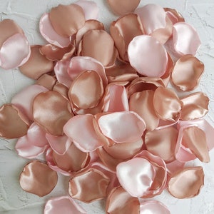 May include: A pile of rose petals in blush pink and rose gold colors. The petals are made of satin fabric and are perfect for weddings, parties, or other special occasions.