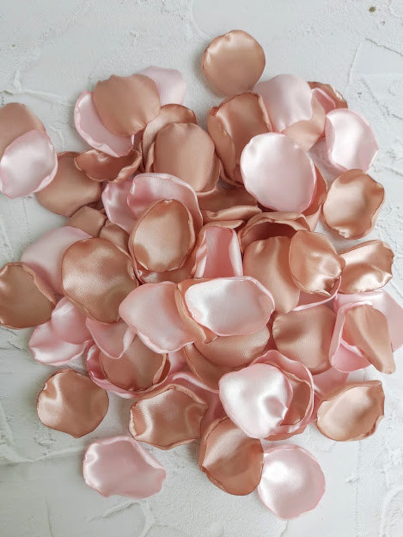 May include: A pile of rose petals in blush pink and rose gold colors. The petals are made of satin fabric and are perfect for weddings, parties, or other special occasions.