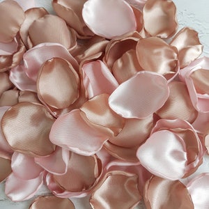 May include: A pile of rose petals in blush pink and rose gold colors. The petals are made of satin fabric and are perfect for weddings, parties, or other special occasions.