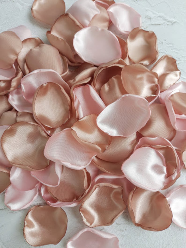 May include: A pile of rose petals in blush pink and rose gold colors. The petals are made of satin fabric and are perfect for weddings, parties, or other special occasions.