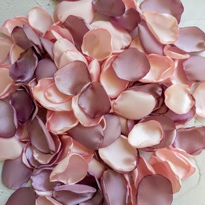 May include: A large pile of pink and mauve silk rose petals. The petals are soft and delicate, perfect for decorating a wedding or special event.