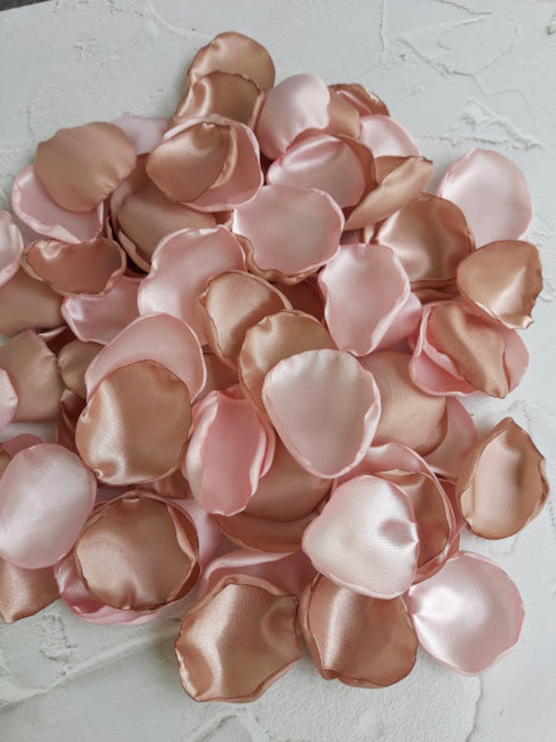 May include: A pile of blush pink satin rose petals. The petals are soft and delicate, perfect for wedding decorations or special events.