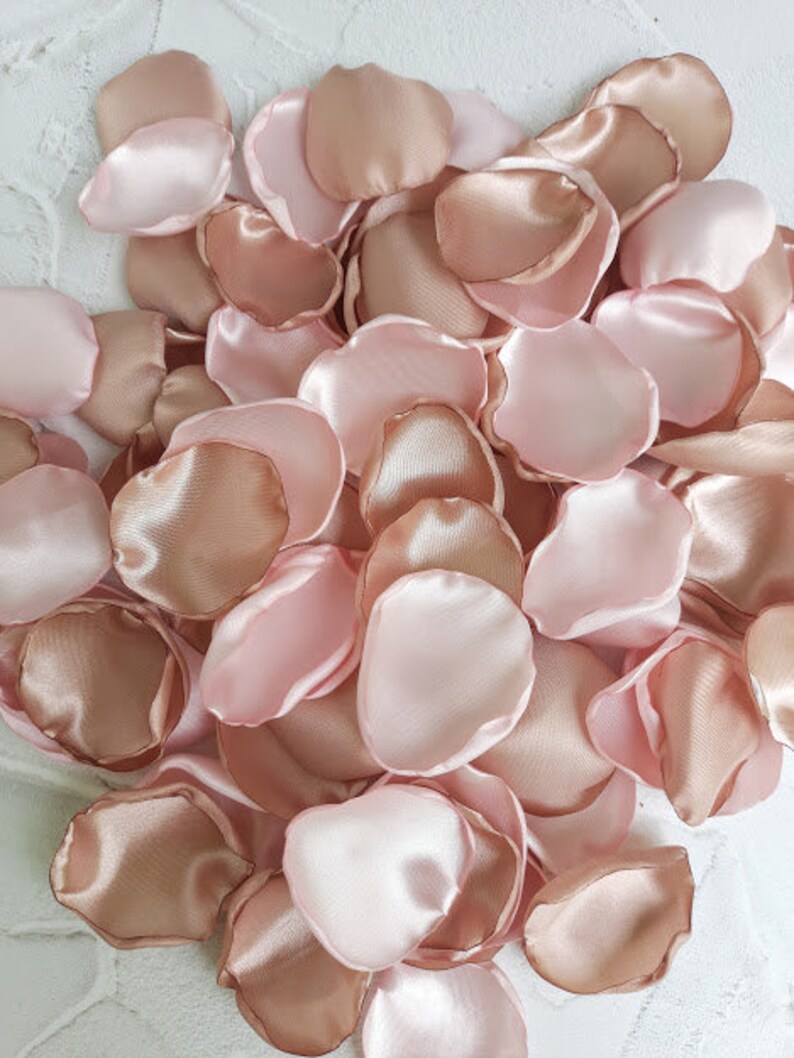 May include: A pile of rose petals in shades of blush pink and champagne. The petals are made of satin fabric and are perfect for weddings, special events, or home decor.