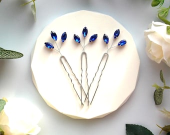 May include: Three silver hair pins with blue crystal accents. Each pin has a small branch design with three blue crystals on each branch.