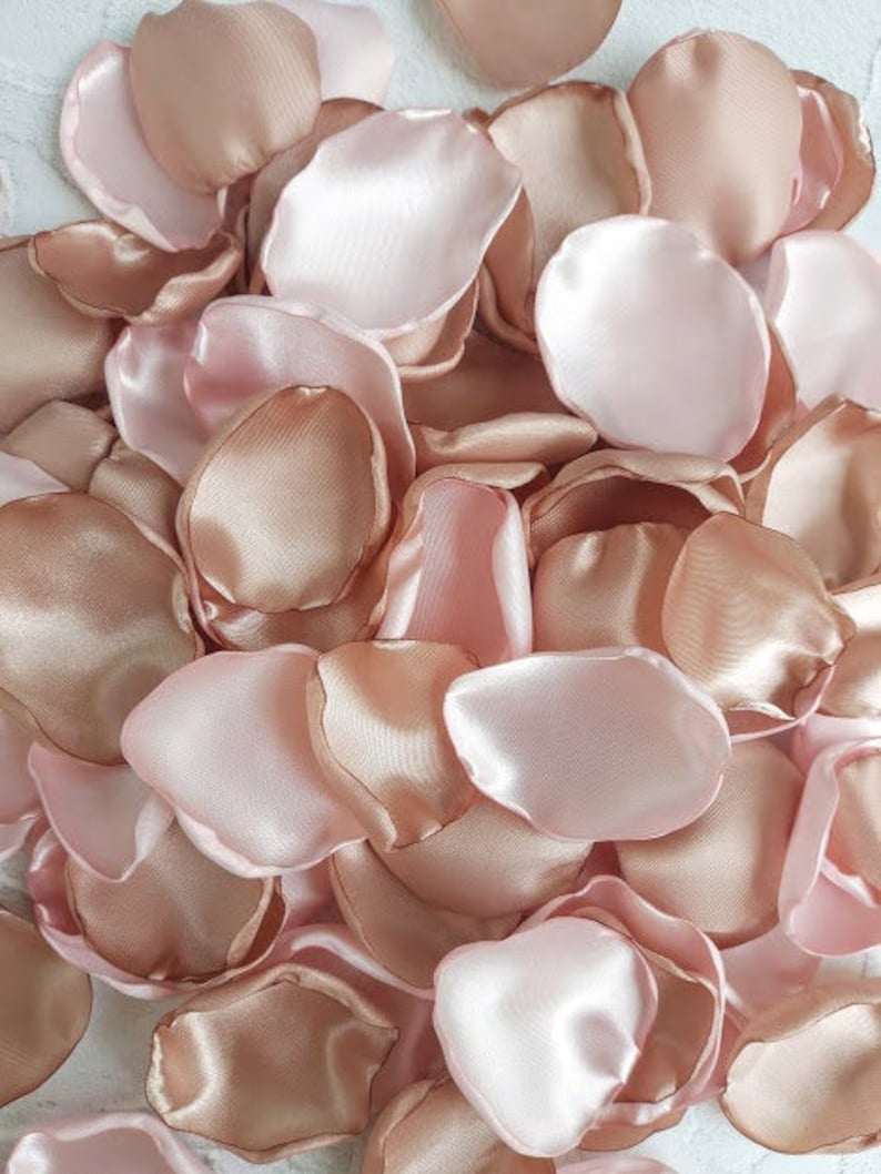 May include: A pile of rose petals in shades of blush pink and champagne. The petals are made of satin fabric and are perfect for weddings, parties, or other special occasions.