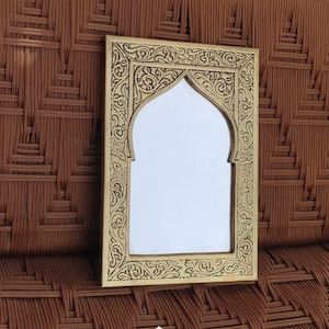 May include: A gold-toned metal mirror with an ornate, arched frame. The frame features intricate floral designs and a Moroccan-inspired style.