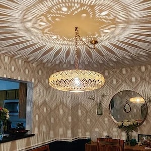 Puede incluir: Un comedor con una mesa y sillas de madera. El techo tiene una l&aacute;mpara decorativa que proyecta una sombra con patr&oacute;n en el techo y las paredes.