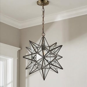 May include: A star-shaped pendant light fixture with a bronze finish. The fixture is suspended from a chain and ceiling mount. The star is constructed of glass panels and metal framing, creating a geometric design. The light bulb is visible inside the star.
