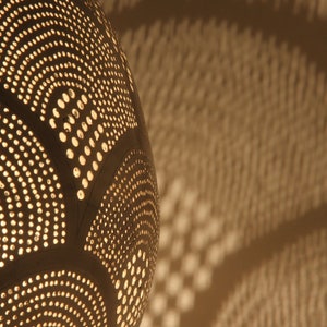 May include: A spherical lamp shade with a dark surface featuring intricate, repeating patterns of small circular perforations. Light shines through these holes, casting a warm, glowing effect and creating a projection of light dots on the surface.