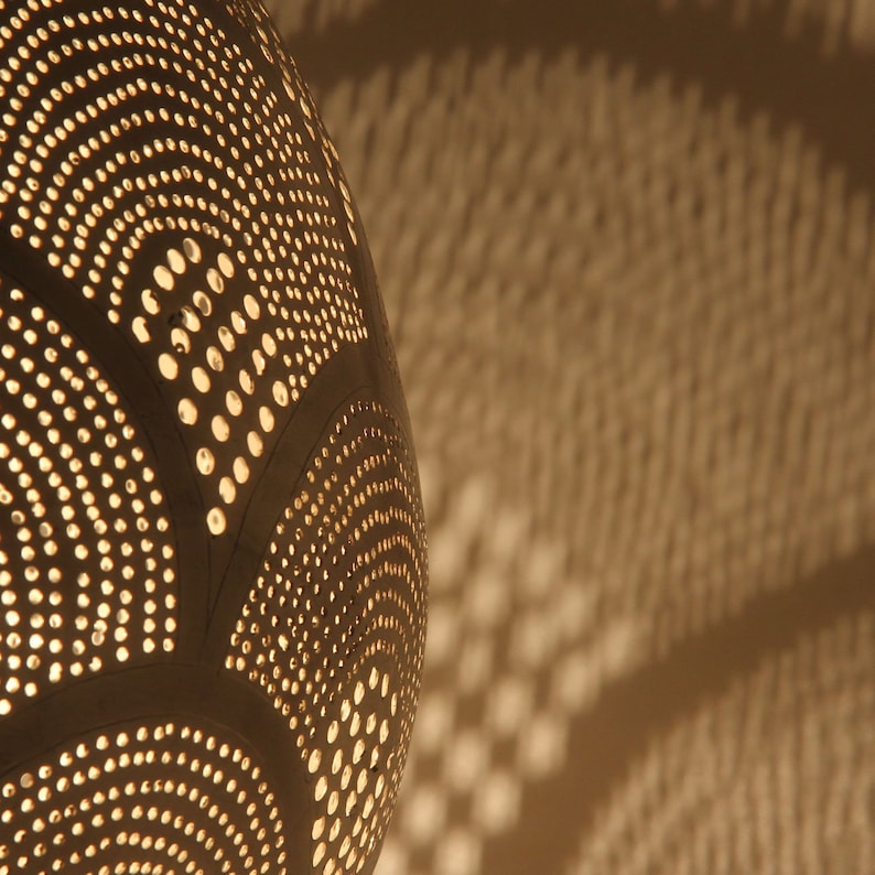 May include: A spherical lamp shade with a dark surface featuring intricate, repeating patterns of small circular perforations. Light shines through these holes, casting a warm, glowing effect and creating a projection of light dots on the surface.