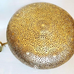 May include: A gold metal ceiling light fixture with a round, intricate, cut-out design. The light fixture has a decorative, ornate pattern.