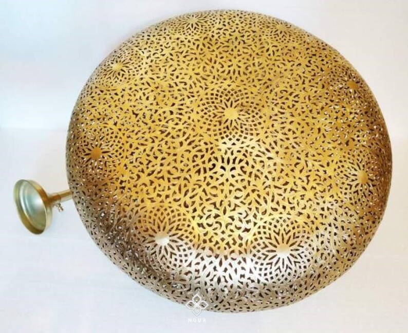 May include: A gold metal ceiling light fixture with a round, intricate, cut-out design. The light fixture has a decorative, ornate pattern.