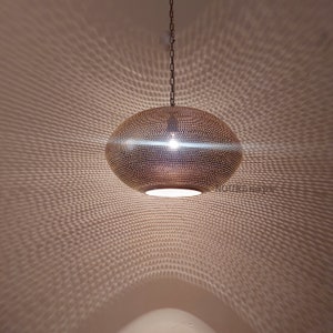 May include: A round, brass pendant light with a perforated design. The light casts a geometric pattern on the ceiling.