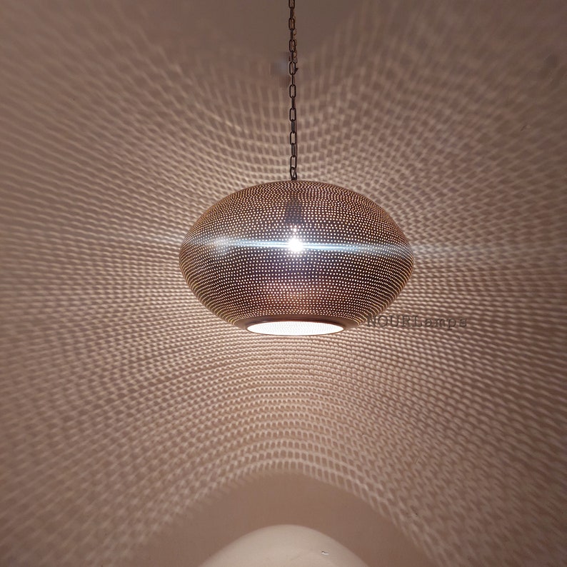 May include: A round, brass pendant light with a perforated design. The light casts a geometric pattern on the ceiling.