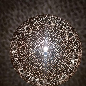 May include: A round, metal, decorative light fixture with a intricate, cut-out pattern. The light fixture is illuminated from the inside, casting a warm glow.