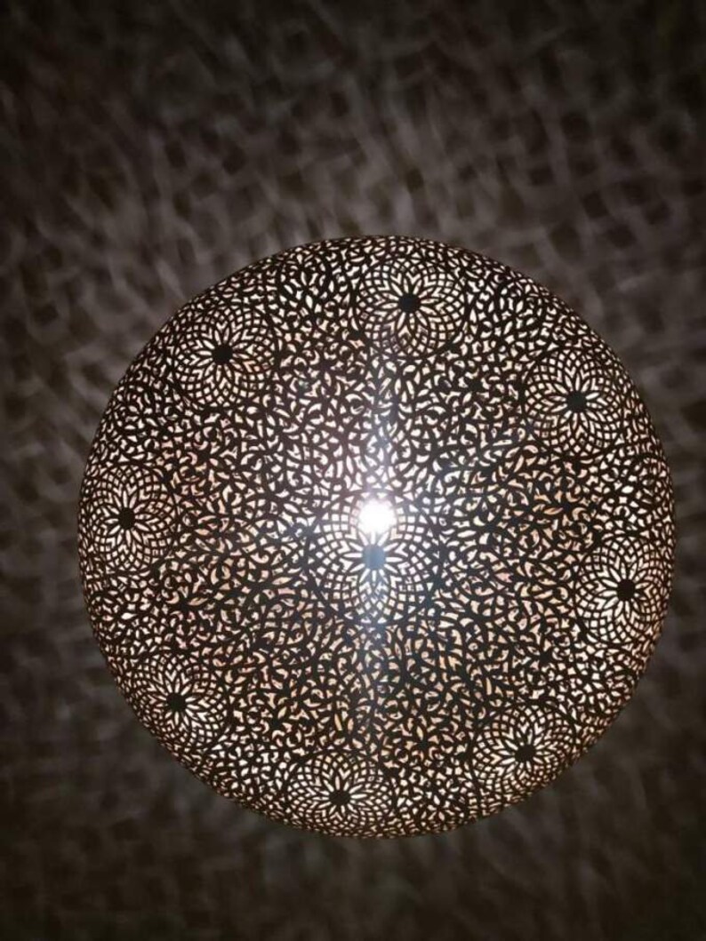 May include: A round, metal, decorative light fixture with a intricate, cut-out pattern. The light fixture is illuminated from the inside, casting a warm glow.