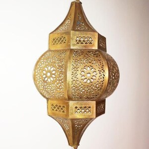 May include: A gold metal Moroccan lantern with intricate cut-out designs. The lantern has a round body and a pointed top.