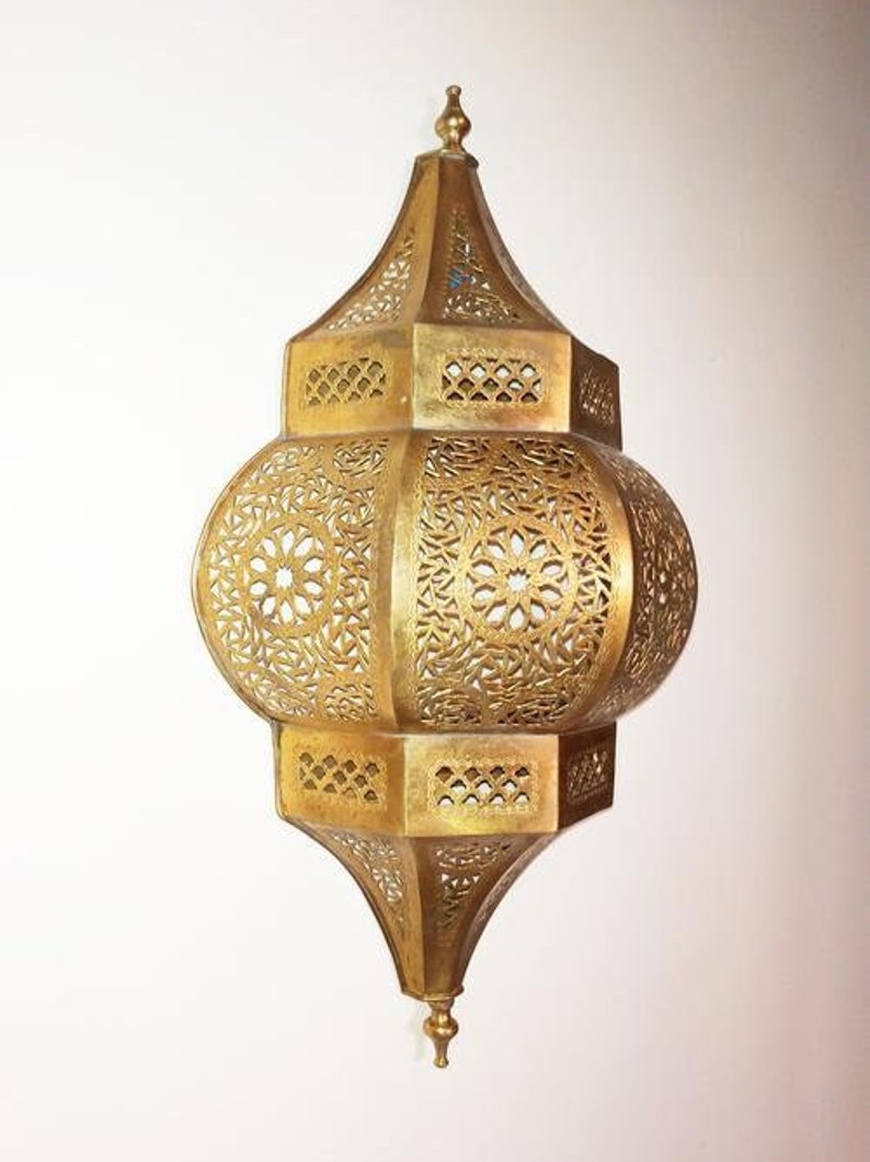 May include: A gold metal Moroccan lantern with intricate cut-out designs. The lantern has a round body and a pointed top.