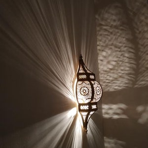 May include: A decorative metal lantern with intricate cutouts and a warm light shining through. The lantern is mounted on a wall and casts a soft glow on the surrounding area.