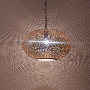 May include: A round, copper-colored pendant light fixture with a perforated design. The light is hanging from a chain and casts a pattern of light on the ceiling.