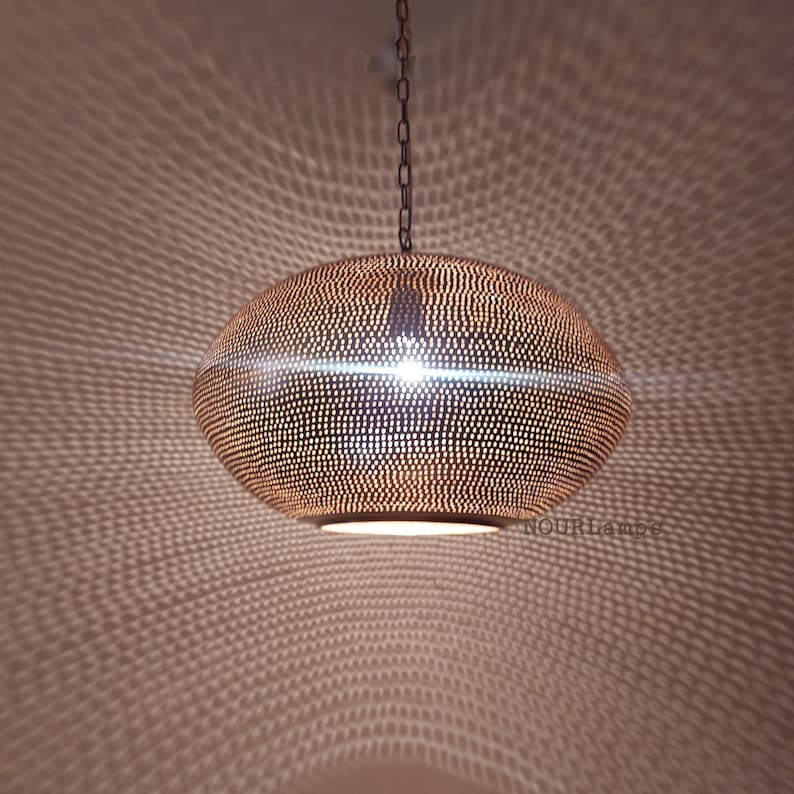 May include: A round, copper-colored pendant light fixture with a perforated design. The light is hanging from a chain and casts a pattern of light on the ceiling.