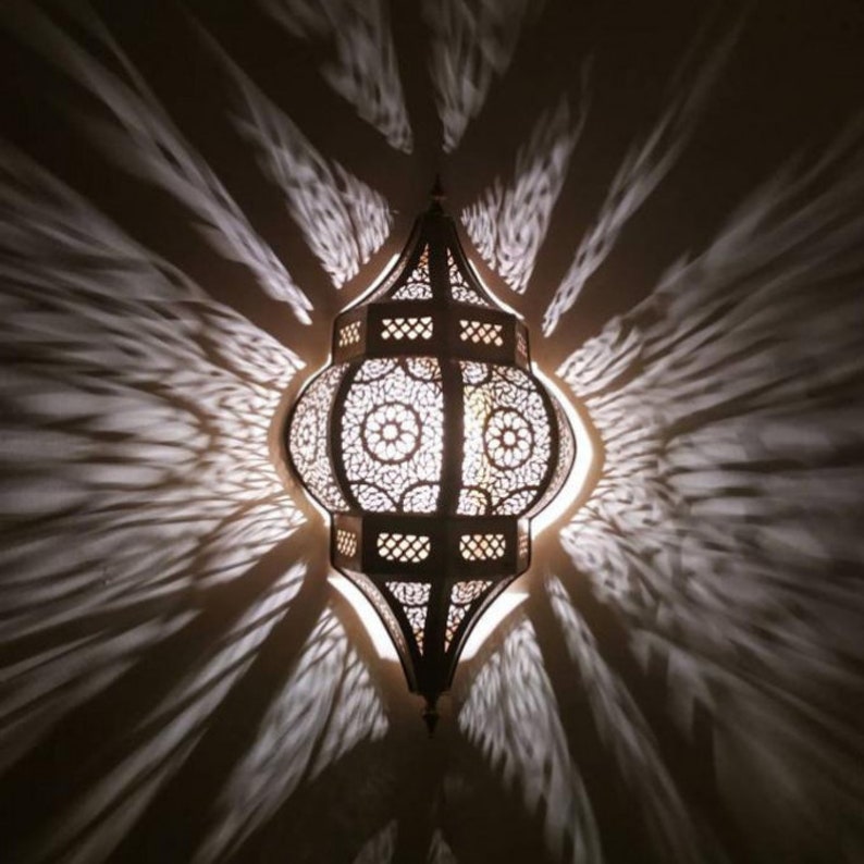 May include: A decorative metal lantern with intricate cutouts and a warm glow. The lantern is hanging from the ceiling and casting intricate shadows on the wall.