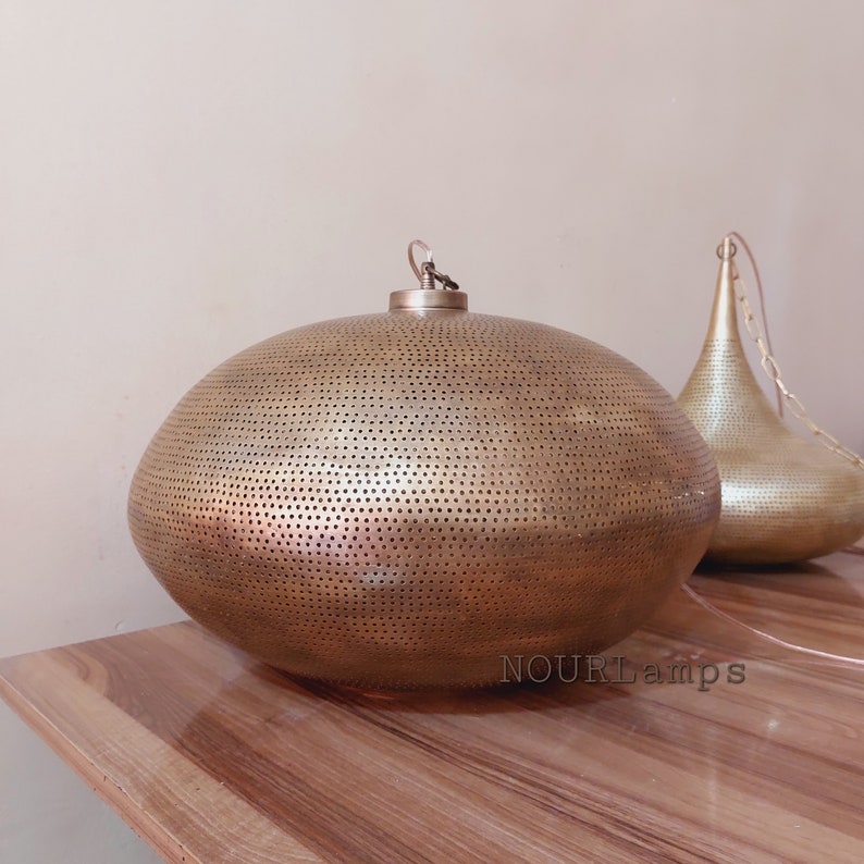 May include: A gold-toned, oval-shaped pendant light fixture with a perforated design. The light fixture is hanging from a chain and has a simple, elegant design.