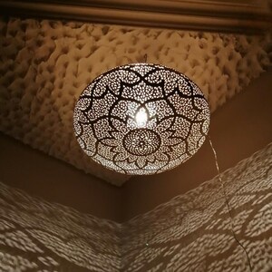 May include: A decorative, spherical pendant light with an intricate, openwork design. The light fixture is suspended from the ceiling and casts patterned shadows on the walls. The light is warm and inviting, creating a cozy atmosphere.