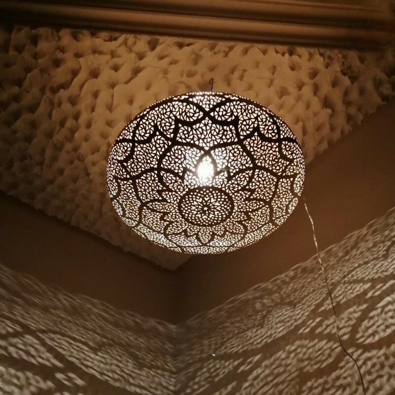 May include: A decorative, spherical pendant light with an intricate, openwork design. The light fixture is suspended from the ceiling and casts patterned shadows on the walls. The light is warm and inviting, creating a cozy atmosphere.