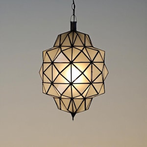 Handmade geometric pendant light with black metal framing and warm glowing panels, creating an elegant modern Moroccan-inspired design.