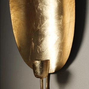 May include: Gold metal wall sconce with a curved, oval-shaped backplate and a single candle holder.