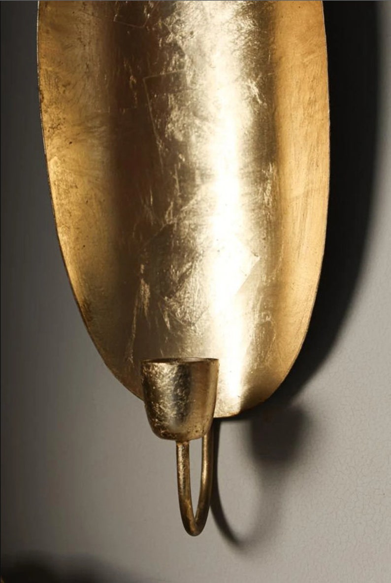 May include: Gold metal wall sconce with a curved, oval-shaped backplate and a single candle holder.