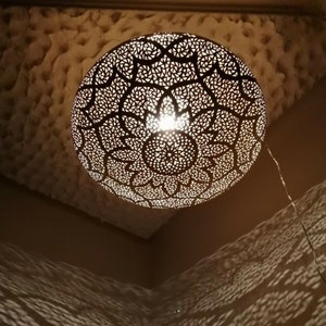 May include: A decorative, spherical pendant light fixture with intricate, geometric cutouts. The light casts patterned shadows on the surrounding walls and ceiling. The fixture is suspended from the ceiling by a wire.