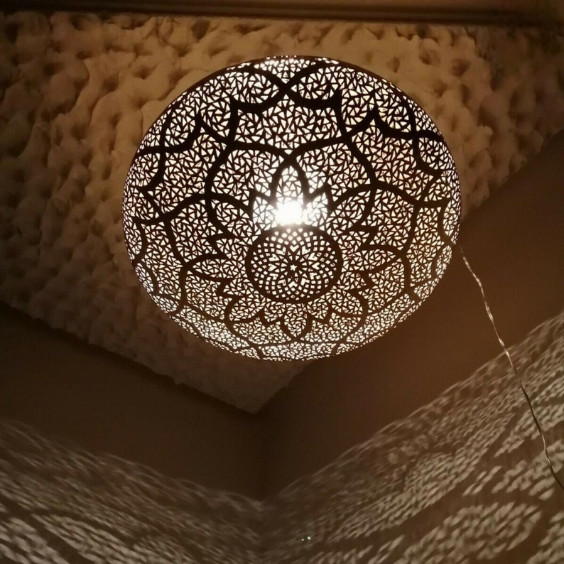 May include: A decorative, spherical pendant light fixture with intricate, geometric cutouts. The light casts patterned shadows on the surrounding walls and ceiling. The fixture is suspended from the ceiling by a wire.