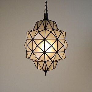 Warm glowing geometric pendant light with intricate black metal framework.