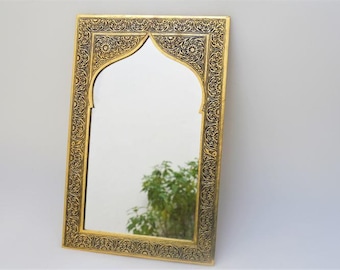 May include: An ornate gold-coloured mirror with a decorative arch design. The mirror has a black background and intricate floral patterns.