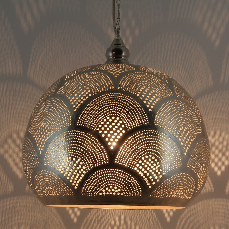 May include: A dome-shaped metal pendant light fixture with a silver finish, featuring a repeating pattern of perforated semi-circles and dots that allow light to pass through, suspended from a matching silver-toned chain and ceiling canopy.