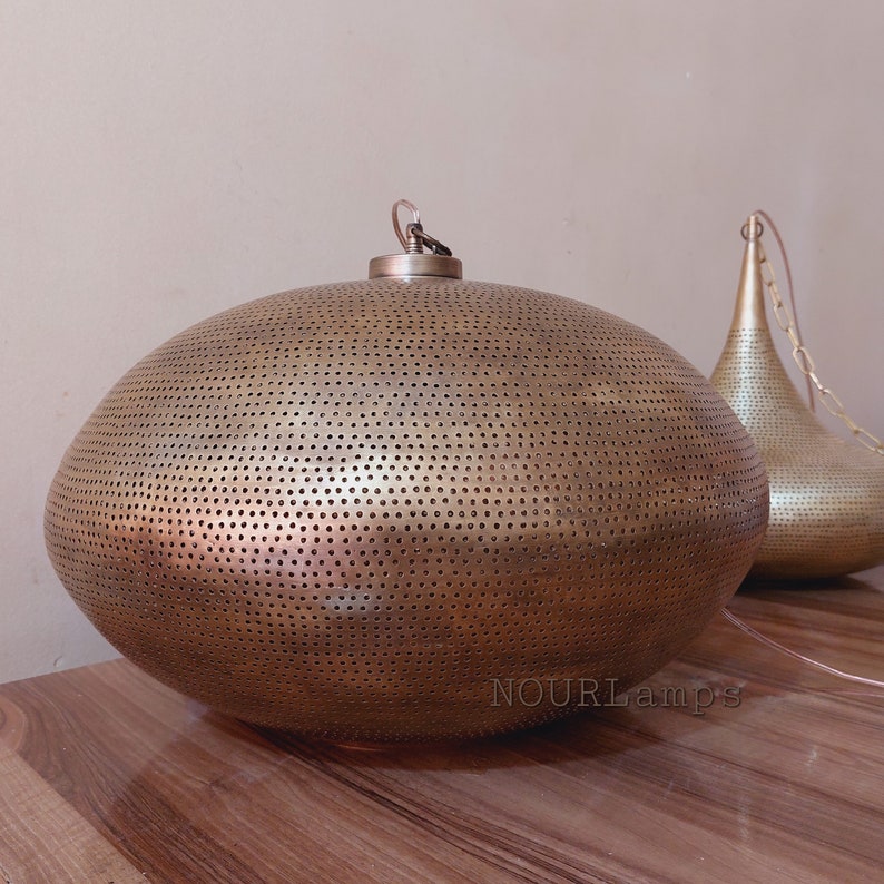 May include: A large, oval-shaped, brass pendant light fixture with a perforated design. The light fixture is hanging from a chain and has a gold finish.