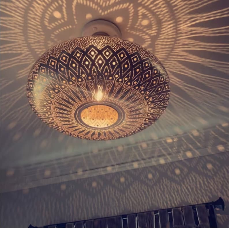 Puede incluir: Una l&aacute;mpara de techo de metal dorado con un patr&oacute;n geom&eacute;trico. La l&aacute;mpara proyecta una sombra decorativa en el techo.