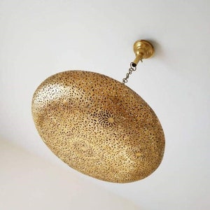May include: A gold-toned, oval-shaped pendant light fixture with intricate cut-out designs. The light fixture is suspended from the ceiling by a chain.