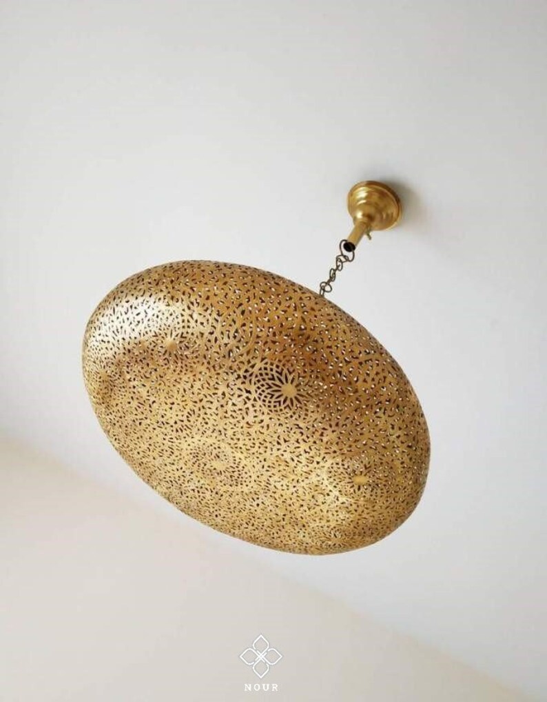 May include: A gold-toned, oval-shaped pendant light fixture with intricate cut-out designs. The light fixture is suspended from the ceiling by a chain.