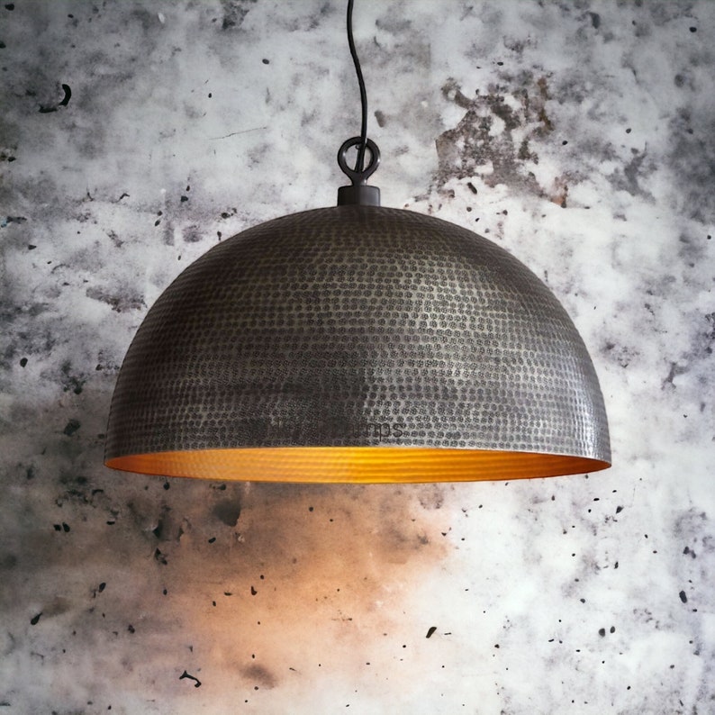 May include: A hammered metal pendant light fixture with a gold interior. The light is hanging from a black cord against a textured gray wall.