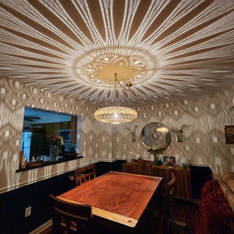 Puede incluir: Un comedor con una mesa y sillas de madera. El techo tiene una l&aacute;mpara decorativa que proyecta una sombra con patr&oacute;n en el techo y las paredes.