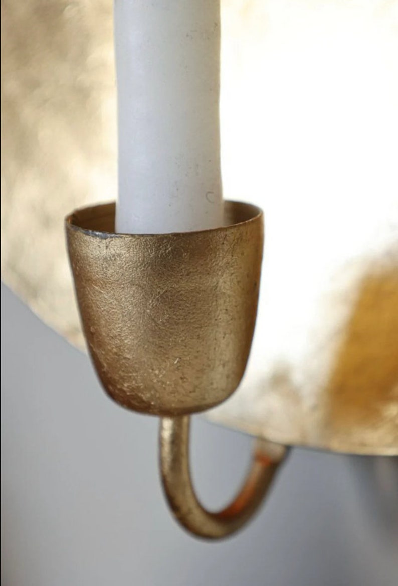 May include: A gold metal candle holder with a white candle. The candle holder has a textured surface and a curved hook.