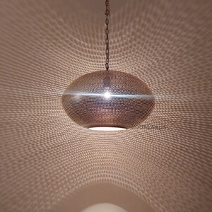 May include: A gold-toned, round, hanging pendant light fixture with a perforated pattern. The light fixture casts a geometric pattern on the ceiling.