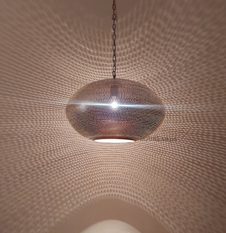 May include: A gold-toned, round, hanging pendant light fixture with a perforated pattern. The light fixture casts a geometric pattern on the ceiling.