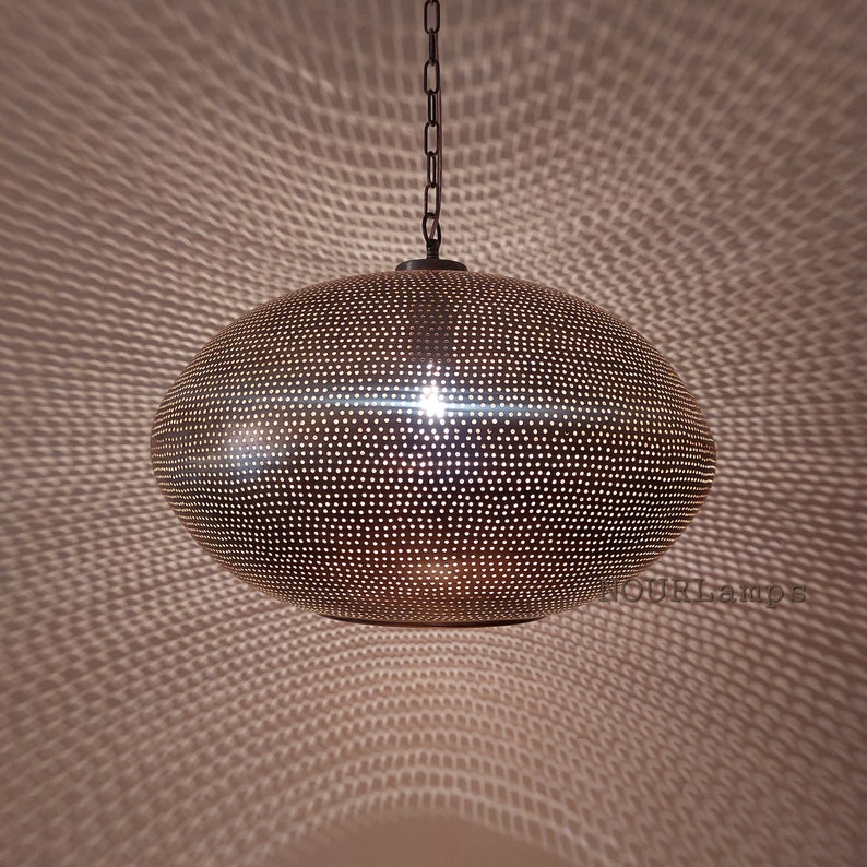May include: A round, brass pendant light with a perforated design. The light is hanging from a chain and casts a patterned shadow on the wall.