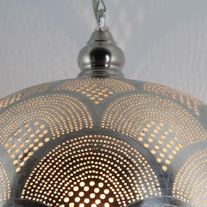 May include: A silver-toned metal pendant light fixture with a dome shape. The surface features an intricate pattern of small, circular perforations arranged in repeating fan-like arcs, allowing light to shine through the metallic material.