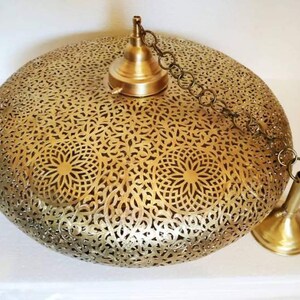 May include: A gold-toned, round, hanging pendant light fixture with a delicate, intricate, cut-out design. The light fixture has a chain and a decorative metal cap.