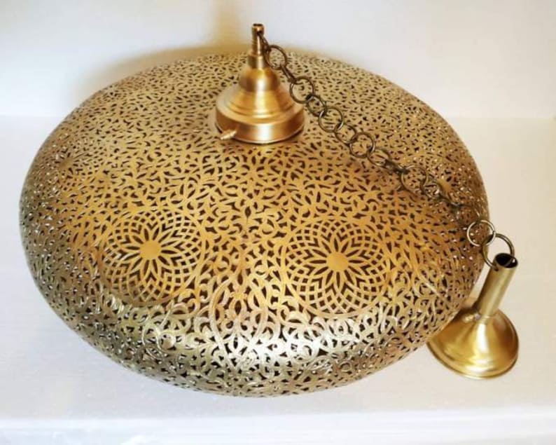 May include: A gold-toned, round, hanging pendant light fixture with a delicate, intricate, cut-out design. The light fixture has a chain and a decorative metal cap.